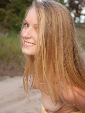 Blonde teen with long legs gets naked in a teasing manner on a sandy road