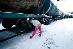 Blonde girl with short hair rips open pink hose in the snow beside a train