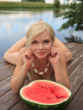 Beautiful blonde Feeona eats a watermelon while posing naked on lakeside dock