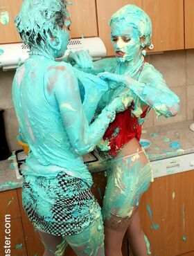 Clothed women cover each other in cake mix during a food fight in kitchen