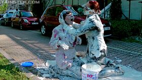 Fully clothed women cover each other in yogurt on a city sidewalk