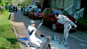 Fully clothed women cover each other in yogurt on a city sidewalk